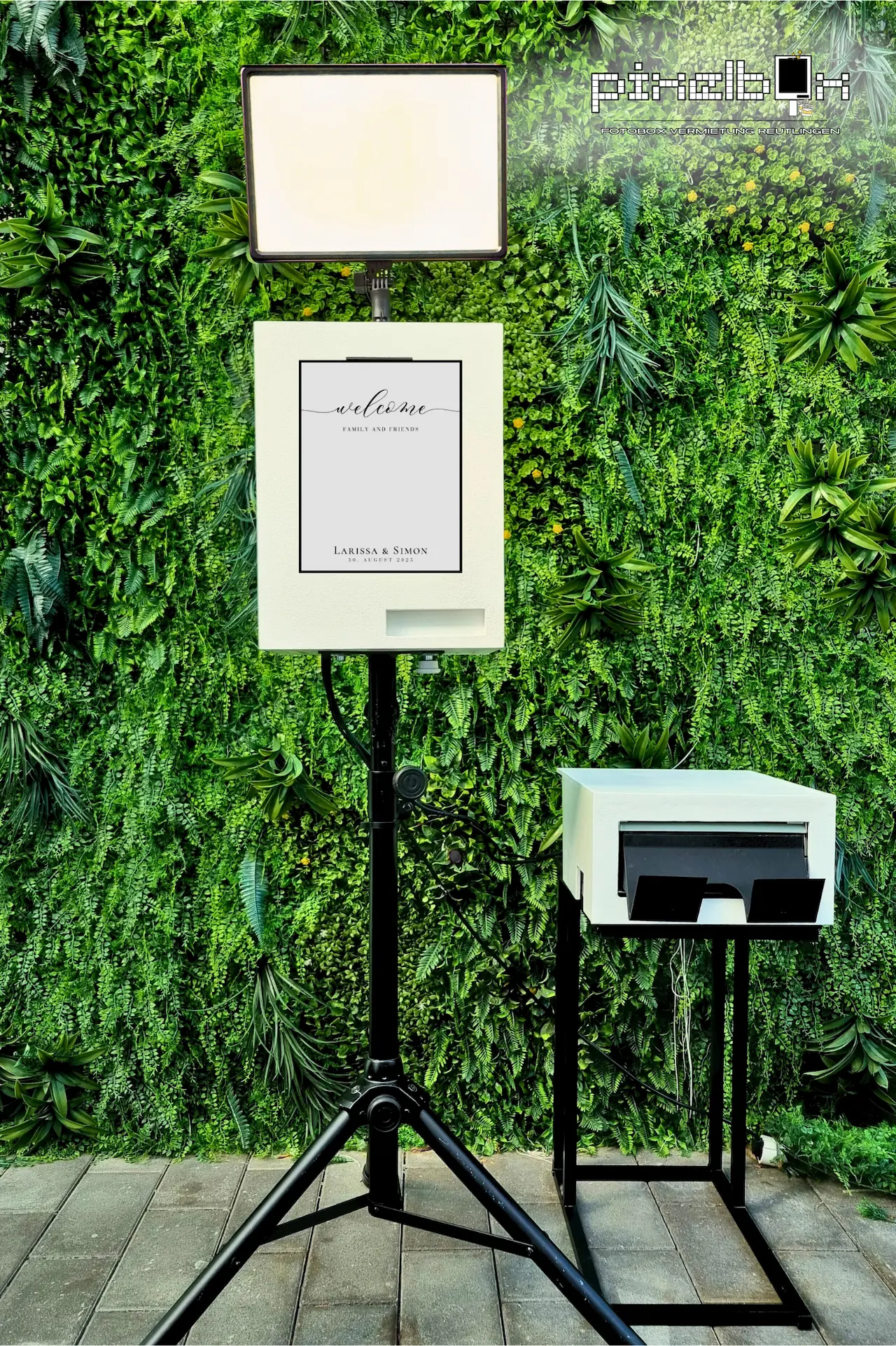 Fotobox mit personalisiertem Willkommensbildschirm vor Pflanzenwand